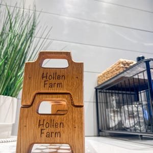 May include: Two stacked wooden crates with the words "Hollen Farm" engraved on each. The crates have a handle on the top and are made of light brown wood.