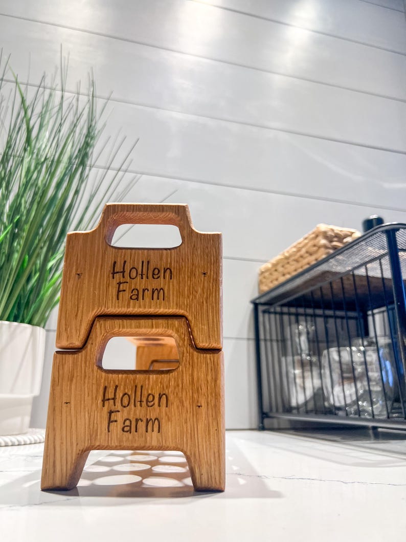 May include: Two stacked wooden crates with the words "Hollen Farm" engraved on each. The crates have a handle on the top and are made of light brown wood.
