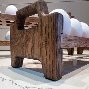 Peut inclure: Un porte-&oelig;ufs en bois avec une teinte brun fonc&eacute;. Le porte-&oelig;ufs a deux niveaux et est fait de bois massif. Le porte-&oelig;ufs est pos&eacute; sur un comptoir blanc.