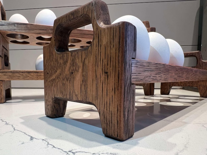 Peut inclure: Un porte-&oelig;ufs en bois avec une teinte brun fonc&eacute;. Le porte-&oelig;ufs a deux niveaux et est fait de bois massif. Le porte-&oelig;ufs est pos&eacute; sur un comptoir blanc.