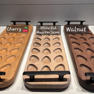 May include: Three wooden serving trays with oval indentations. The trays are made of cherry, white oak, and walnut. Each tray has a black handle at each end. The cherry tray has the word "Cherry" on it.