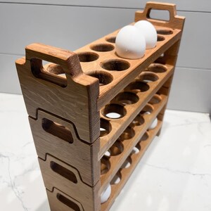 May include: A wooden egg crate with three tiers, each holding 12 egg slots. Two white eggs are in the top tier.