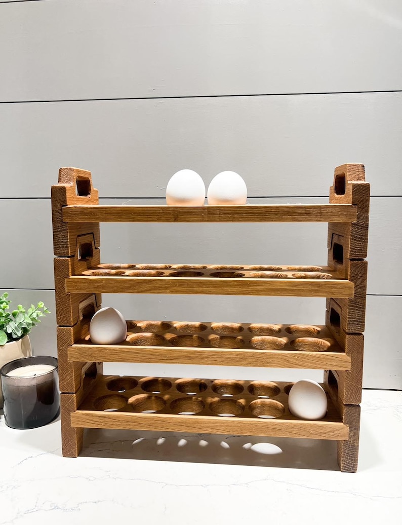 May include: A wooden egg holder with four shelves, each with 12 egg slots. The holder is made of natural wood and has a rustic look. There are three white eggs on the top shelf.
