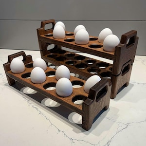 May include: Two wooden egg crates stacked on top of each other. The top crate has 12 white eggs in it, and the bottom crate has 10 white eggs in it.