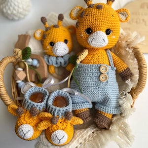 May include: A set of handmade crochet items in a wicker basket, including a giraffe doll wearing light blue overalls with wooden buttons, a smaller giraffe rattle with a blue ruffled collar, and a pair of yellow giraffe-themed baby booties.