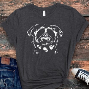 May include: A dark heather grey t-shirt with a white silhouette of a pug wearing sunglasses. The pug is looking directly at the viewer.