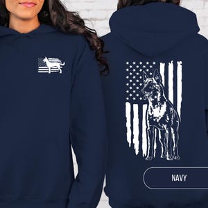 May include: A navy blue hooded sweatshirt featuring a white graphic of a dog silhouette over a distressed American flag on the left chest, and a larger white graphic of a dog standing in front of a distressed American flag on the back.