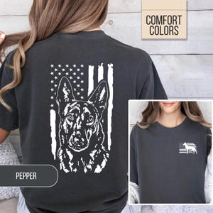 May include: A charcoal gray t-shirt featuring a large white graphic on the back of a German Shepherd dog head superimposed over a stylized American flag. The front left chest area displays a smaller white graphic of a dog silhouette and flag.