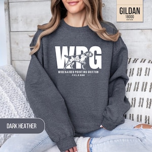May include: A dark heather gray crewneck sweatshirt featuring a white graphic print. The design displays the large letters WPG with a silhouette of a Wirehaired Pointing Griffon dog in the center, followed by the text WIREHAIRED POINTING GRIFFON FIELD DOG.