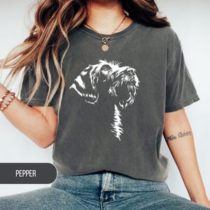 May include: Dark gray t-shirt featuring a white graphic of a dog's head. The dog is looking upwards. The word "PEPPER" is printed on a dark gray rectangle at the bottom of the image.