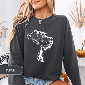 May include: Dark gray sweatshirt featuring a white graphic of a dog's head. The word "PEPPER" is printed on a dark gray rectangle at the bottom left. The sweatshirt has long sleeves and a crew neck.