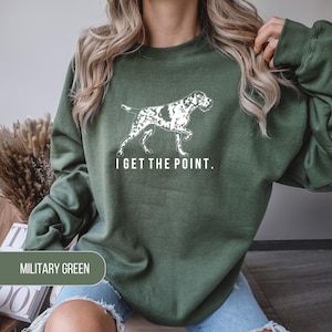 May include: A military green crewneck sweatshirt featuring a white graphic of a pointing dog in profile. Below the dog, the text reads I GET THE POINT. in a clean, sans-serif font. The garment has long sleeves and a ribbed collar and cuffs.