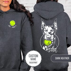 May include: Dark heather gray hoodie with a tennis ball graphic on the front and a Doberman Pinscher with a tennis ball graphic on the back. The front says "Just Throw It." The back has the name "Diesel" below the dog.