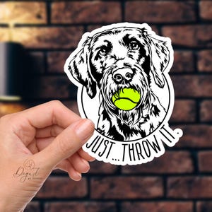 May include: Black and white illustration of a dog with a tennis ball in its mouth. The dog is looking directly at the viewer. The text "Just...Throw It." is written below the dog.