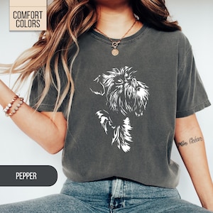 May include: Dark grey t-shirt with a white illustration of a dog's face. The shirt has the words "Comfort Colors" in a box in the upper left corner and the word "Pepper" in a box at the bottom. The shirt is made of a soft, comfortable material.