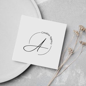 May include: A white card with a black circle containing a stylised letter A and the text "Creative Agency" in a circle around the letter.
