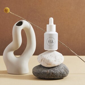 May include: A white bottle with a dropper top and a label that says "Creative Energy Serum" and "ea" in a circle. The bottle is sitting on top of a stack of three grey and white stones.