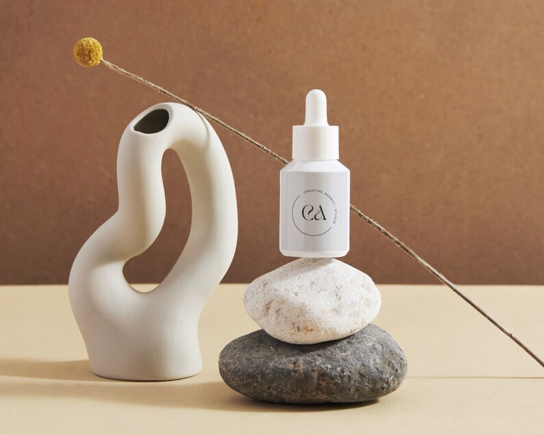 May include: A white bottle with a dropper top and a label that says "Creative Energy Serum" and "ea" in a circle. The bottle is sitting on top of a stack of three grey and white stones.