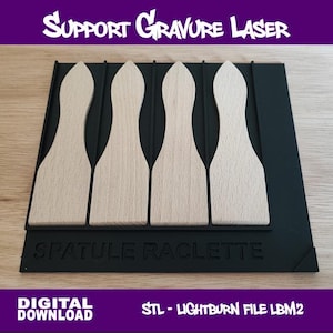 Op de afbeelding: Een zwarte lasergravure-ondersteuning met vier houten spatels. De spatels zijn lichtbruin en hebben een unieke vorm. De basis heeft de tekst "SUPPORT GRAVURE LASER" en "SPATULE RACLETTE". De afbeelding bevat ook de tekst "DIGITAL DOWNLOAD".