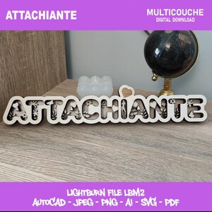 May include: A wooden sign that reads "ATTACHIANTE" in a decorative font, with floral cutouts within the letters. The sign is on a wooden surface, with a small globe and other decorative items in the background.