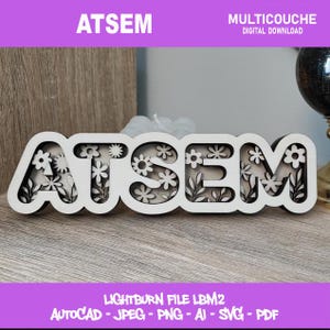 Peut inclure: Un panneau en bois multicouche avec le mot "ATSEM" en blanc, orné de motifs floraux et d'un intérieur noir. Le panneau est posé sur une surface en bois. Le texte "MULTICOUCHE DIGITAL DOWNLOAD" est au-dessus. Le texte "LIGHTBURN FILE LBM2 AUTOCAD - JPEG - PNG - AI - SVG - PDF" est en dessous.