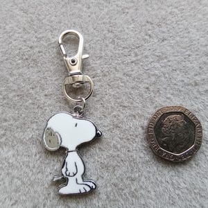 May include: A silver keychain featuring a cartoon Snoopy character. The keychain has a silver split ring and a silver lobster clasp.