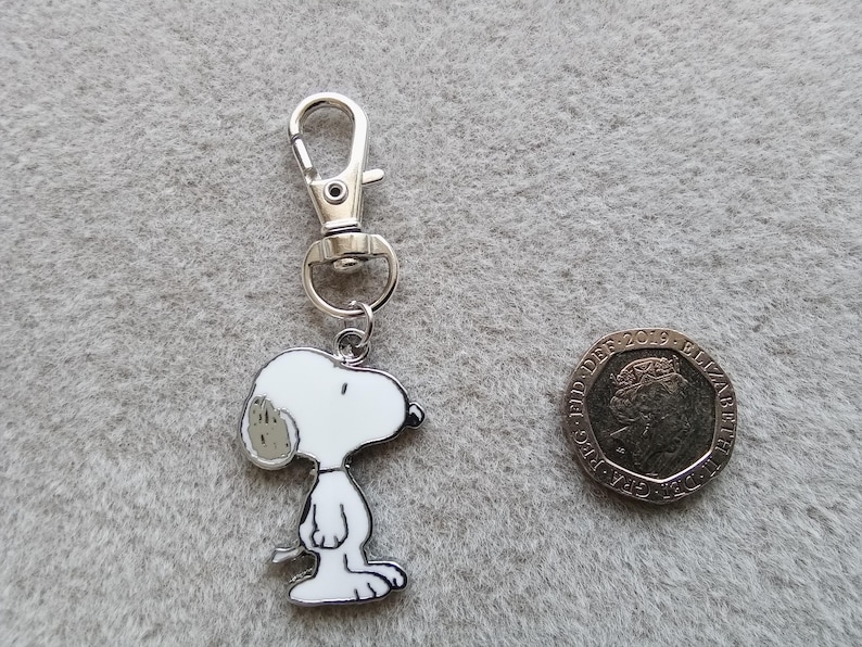 May include: A silver keychain featuring a cartoon Snoopy character. The keychain has a silver split ring and a silver lobster clasp.