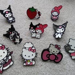 May include: A selection of enamel pins depicting cartoon characters. The pins feature characters in diverse poses and attire, with a colour scheme including black, white, red, and pink. The pins are likely for decorative use.