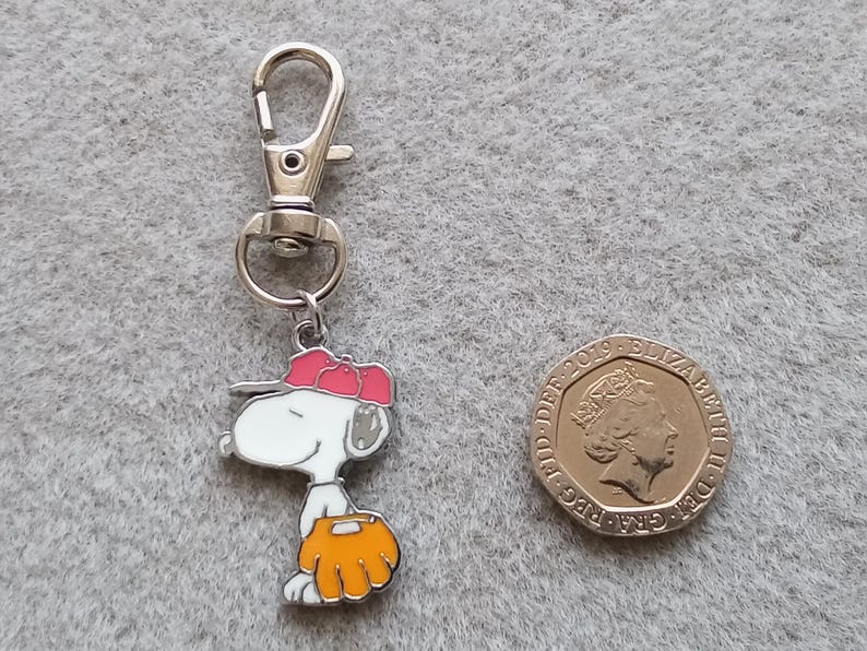 May include: A silver keychain with a cartoon character wearing a red baseball cap and holding a baseball glove. The character is white with black eyes and a black nose. The keychain is attached to a silver ring.