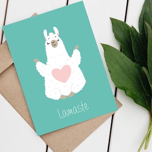 Op de afbeelding: Een turquoise kaart met een witte lama die een roze hart draagt en yoga doet. De kaart zegt "Lamaste" in witte tekst.