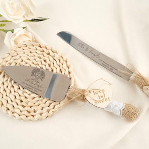 May include: A silver cake server and knife set for a 50th wedding anniversary. The server and knife have wooden handles wrapped in burlap and lace. The server has the text "Pete & Angela 50th Wedding Anniversary August 10, 1975". A wooden heart tag reads "love is sweet".