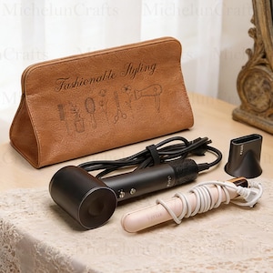 May include: A brown leatherette pouch with the words "Fashionable Styling" and hair styling tools etched on it. A black hair dryer, a black nozzle, and a pink and white flat iron are also in the image.