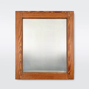 May include: A rectangular wooden mirror with a simple frame. The frame is made of natural wood with a light brown stain. The mirror is reflecting a blurry image.
