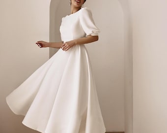 May include: A solid white midi-length dress featuring a round neckline, short puff sleeves, and a full, flared skirt that falls below the knees. The garment is constructed with a fitted bodice and a clean, unadorned finish throughout the fabric.