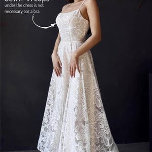A woman wearing a white lace dress with a high neckline and a long skirt, posing against a dark background.
