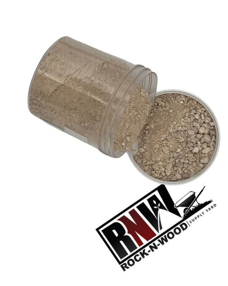 May include: A clear plastic container filled with light brown gravel. The container is tipped over, spilling the gravel onto a white surface. The container has a label that reads "ROCK-N-WOOD SUPPLY YARD".