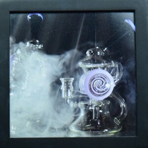May include: A glass water pipe with a purple spiral design and a clear glass base. The pipe is surrounded by smoke.