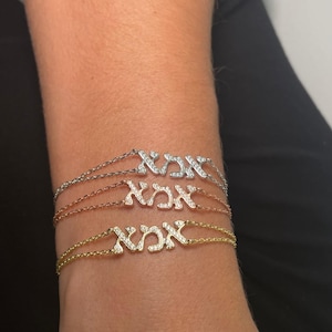 Könnte beinhalten: Drei zarte Armbänder mit einem hebräischen Wort, das mit Pavé-Diamanten besetzt ist. Die Armbänder sind in Silber, Roségold und Gold.