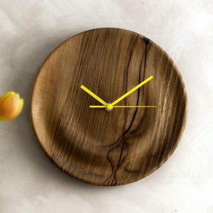 May include: A wooden wall clock with a dark brown wood grain finish and bright yellow hands.