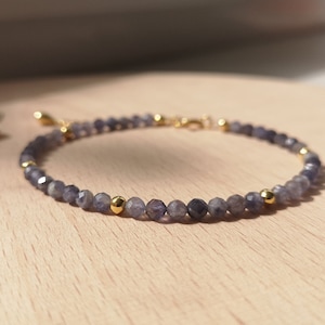 Può includere: Un braccialetto delicato realizzato con piccole pietre preziose sfaccettate di colore grigio scuro e dettagli dorati.