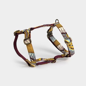 Op de afbeelding: Een hondenharnas met een bordeauxrood en geel patroon en goudkleurige hardware.