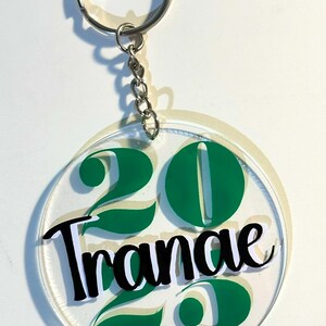 May include: Clear acrylic keychain with a silver chain and ring. The keychain features the number "20" in green, with the name "Tranae" in black script. Green leaf accents are also present.