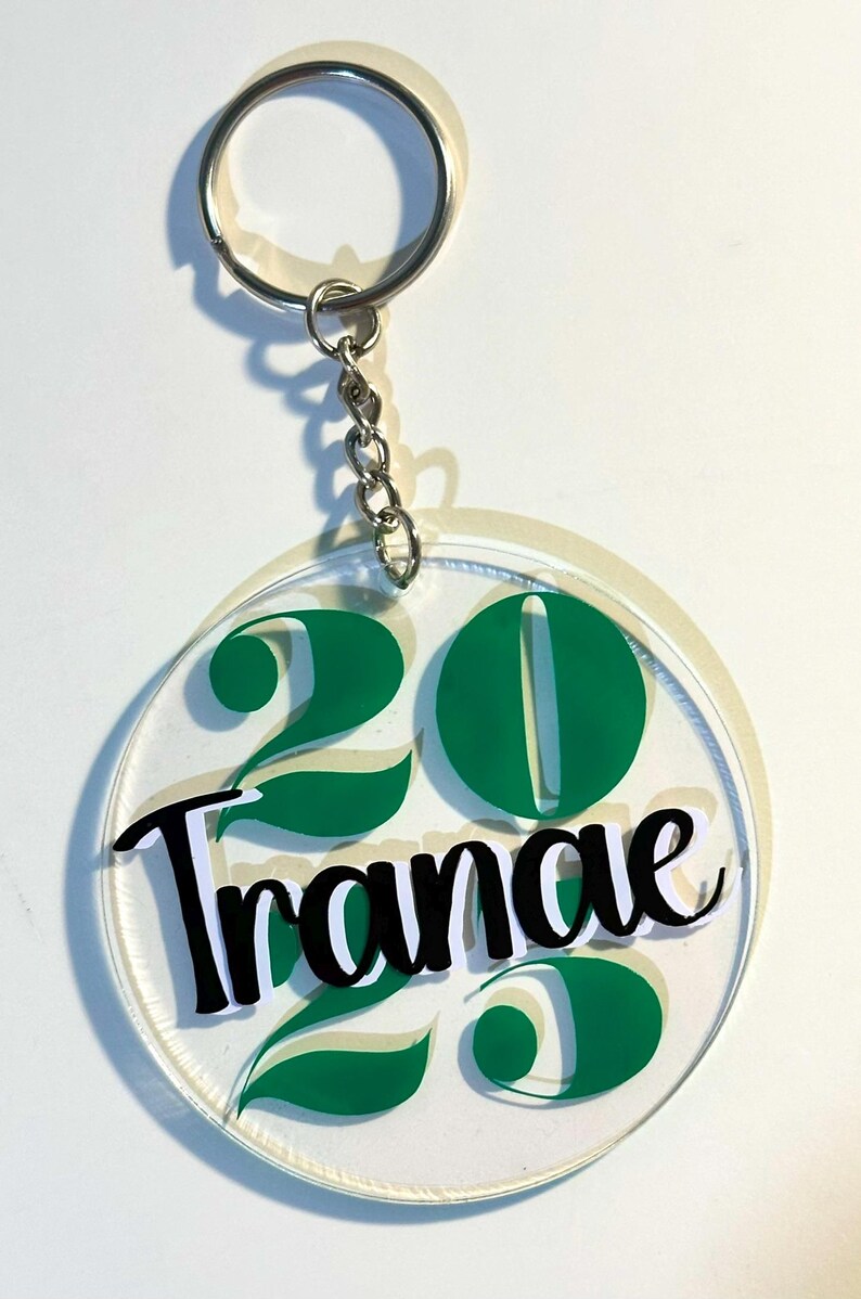 May include: Clear acrylic keychain with a silver chain and ring. The keychain features the number "20" in green, with the name "Tranae" in black script. Green leaf accents are also present.
