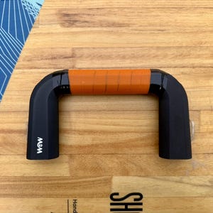 May include: A black handle with an orange grip, labeled "MWM" on the side. The handle is on a wooden surface.