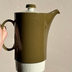 May include: A brown and white ceramic coffee pot with a lid and a handle. The pot has a white band around the bottom and a white knob on the lid.