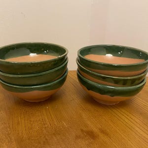 May include: Set of two stacks of four green and orange ceramic bowls. Each bowl has a green rim and a light orange interior.