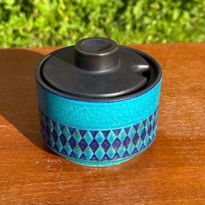 May include: A blue and black ceramic sugar bowl with a lid. The bowl has a geometric pattern of diamonds.