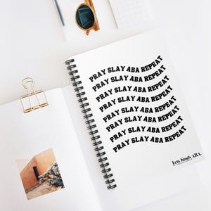 May include: A white spiral notebook with the text "Pray Slay Aba Repeat" repeated in black text in a curved pattern. The text "Lets Stundy ABA." is printed in black at the bottom of the notebook.