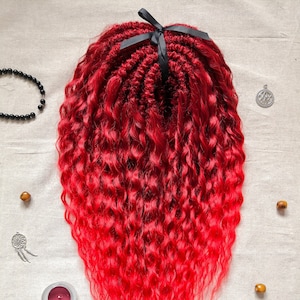 Könnte beinhalten: Eine lange, rote, lockige Perücke mit einem schwarzen Band, das oben gebunden ist. Die Perücke ist in einem geflochtenen Muster gestylt.