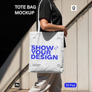 Puede incluir: Maqueta de bolso tote blanco con el texto "SHOW YOUR DESIGN" en azul. El bolso tiene una correa blanca y lo sostiene una persona. También son visibles las palabras "TOTE BAG MOCKUP". La imagen también incluye el texto "ESTD 2025" y "WHAT YOU GET".